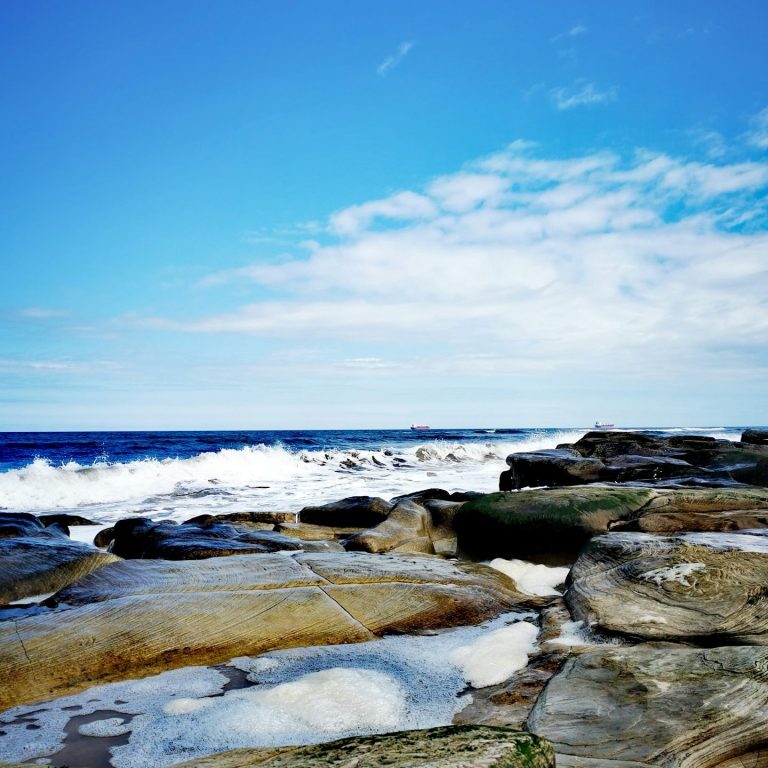 Felsen am Meer unter einem klaren blauen Himmel mit sanften Wellen.